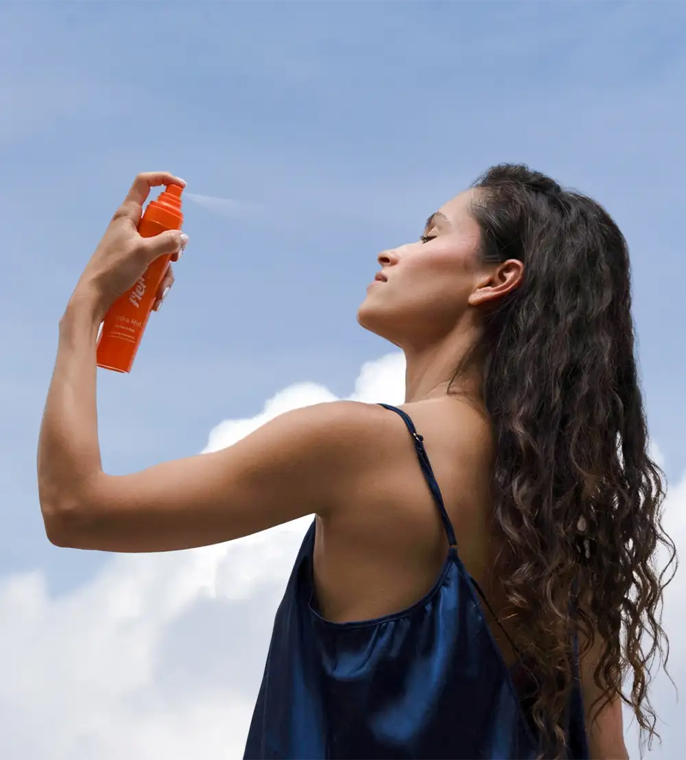 Woman applying body mist spray against a blue sky